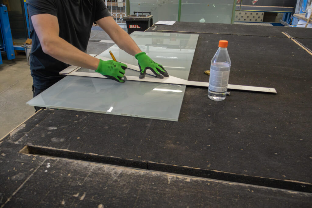 Glasschneiden in der Werkstatt – Handwerker schneidet Glasscheibe mit Schneidwerkzeug